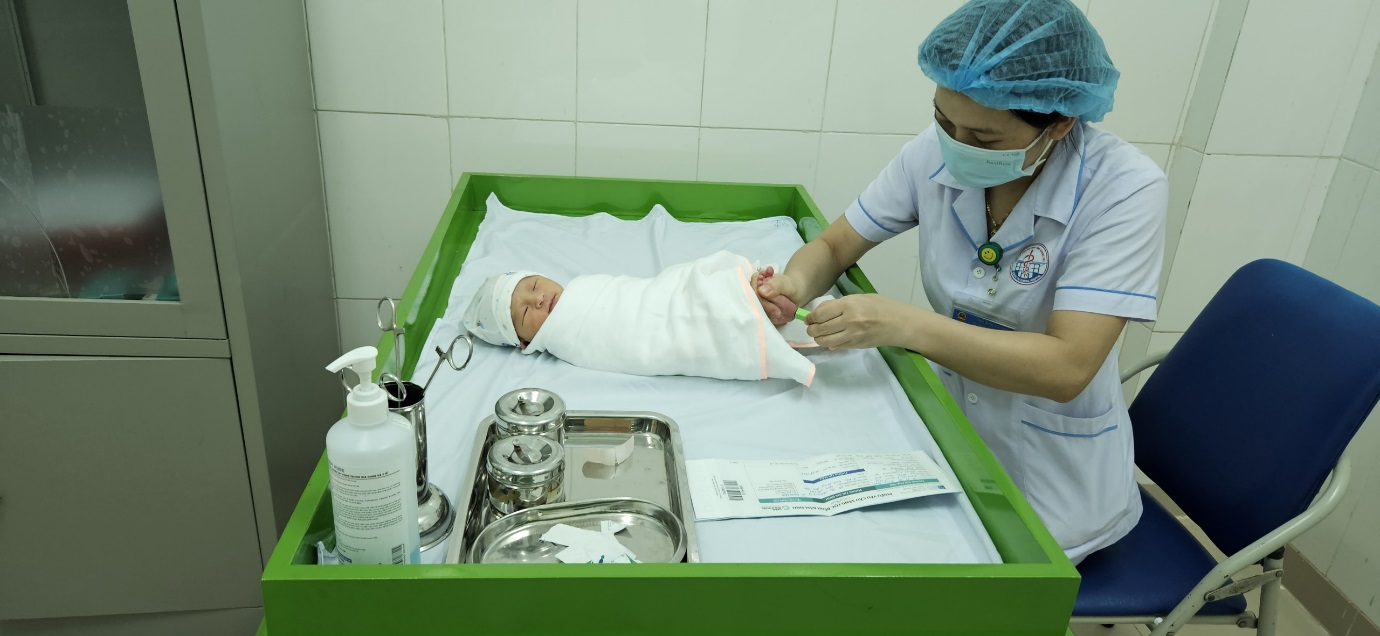 Nhân viên y tế đang lấy máu gót chân cho bé thực hiện xét nghiệm